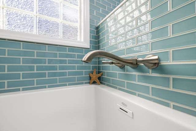 Pale blue glass subway tile around a bathtub, with a brushed-nickel wall-mounted faucet.