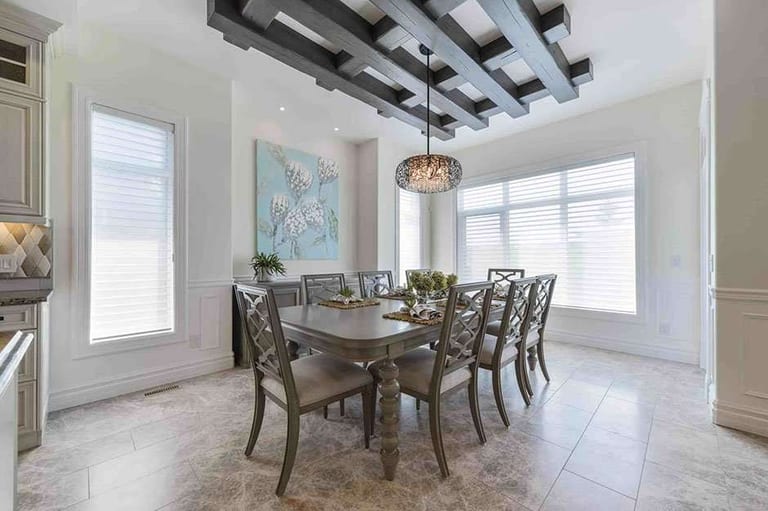 White cellular shades on the windows of a formal dining room, above a large-format porcelain tile floor, under a dark timber ceiling grid.