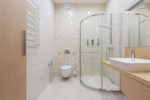 A bathroom with a curved glass shower enclosure, a wall-hung toilet and pale large-format tile.