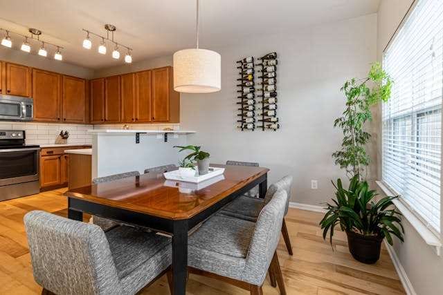 A dining area with a pale wood floor and grey upholstered chairs, with a wood-cabinet kitchen behind.
