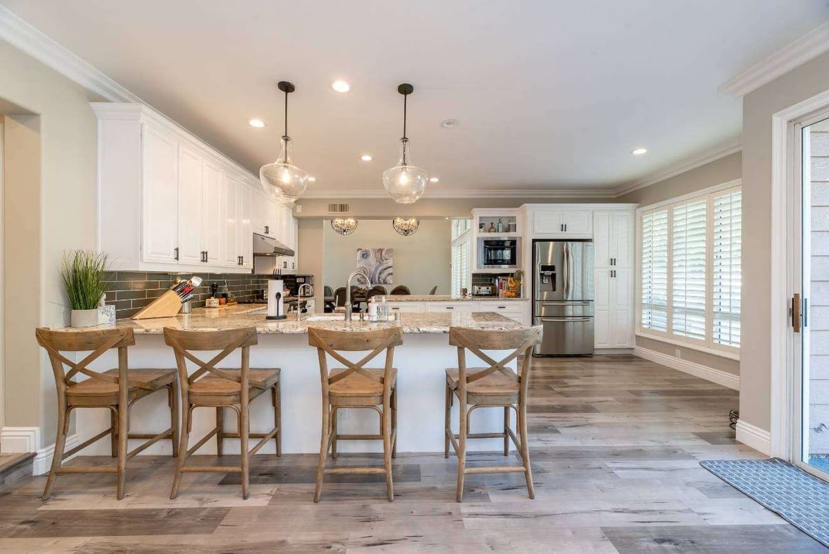 Grey wood-look plank flooring in an open kitchen with a white island, wicker-backed stools and glass pendant lights