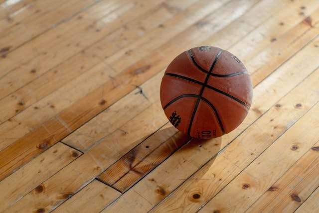A basketball resting on worn wood strip flooring.