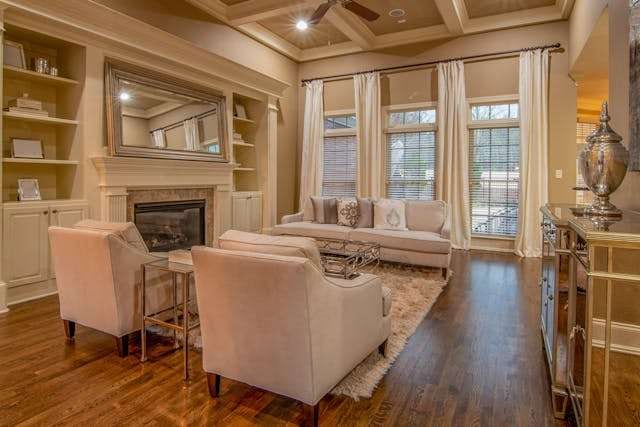 A formal living room with a dark hardwood floor, cream armchairs, a fireplace and built-in shelving.