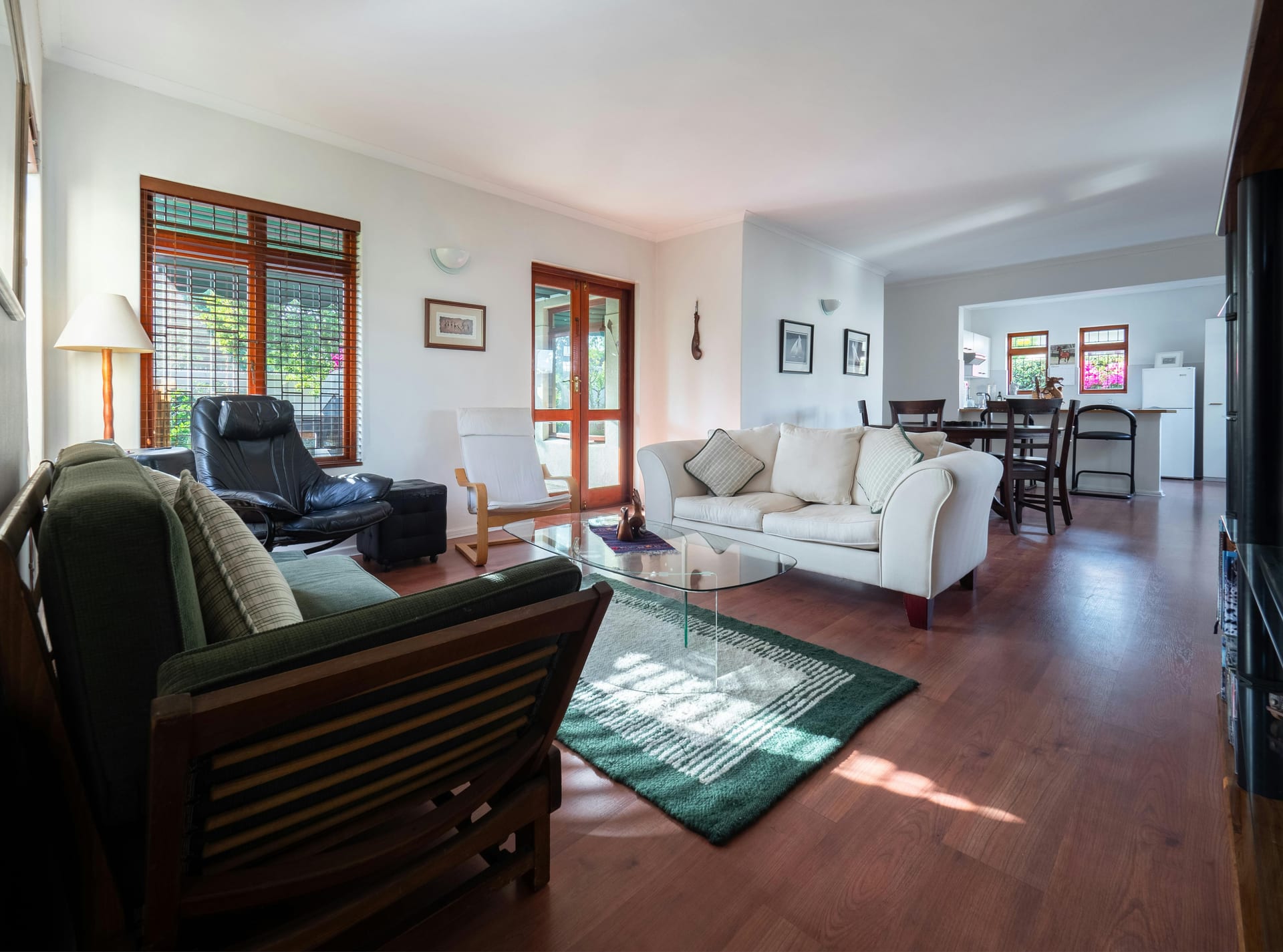 An open living and dining room with a warm reddish hardwood floor and a green area rug.