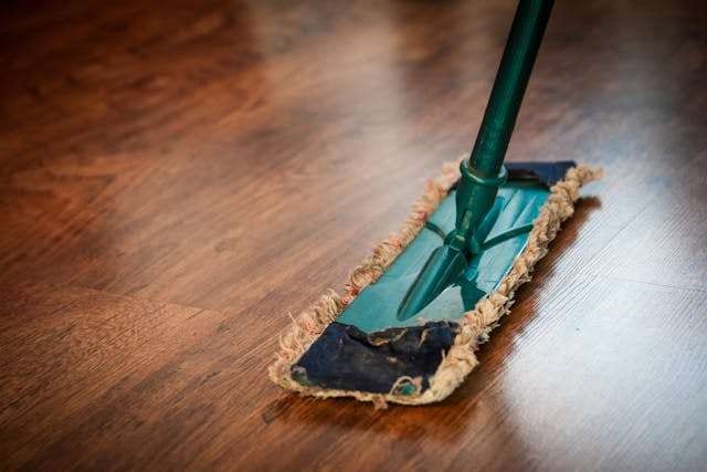 A flat microfibre mop cleaning a glossy dark wood floor.