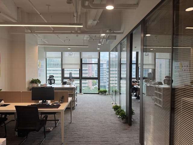An open-plan office with grey carpet tile, desks and glass-walled meeting rooms.