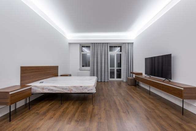 A bedroom with dark wood-look plank flooring, a wooden bed frame and a wall-mounted TV.