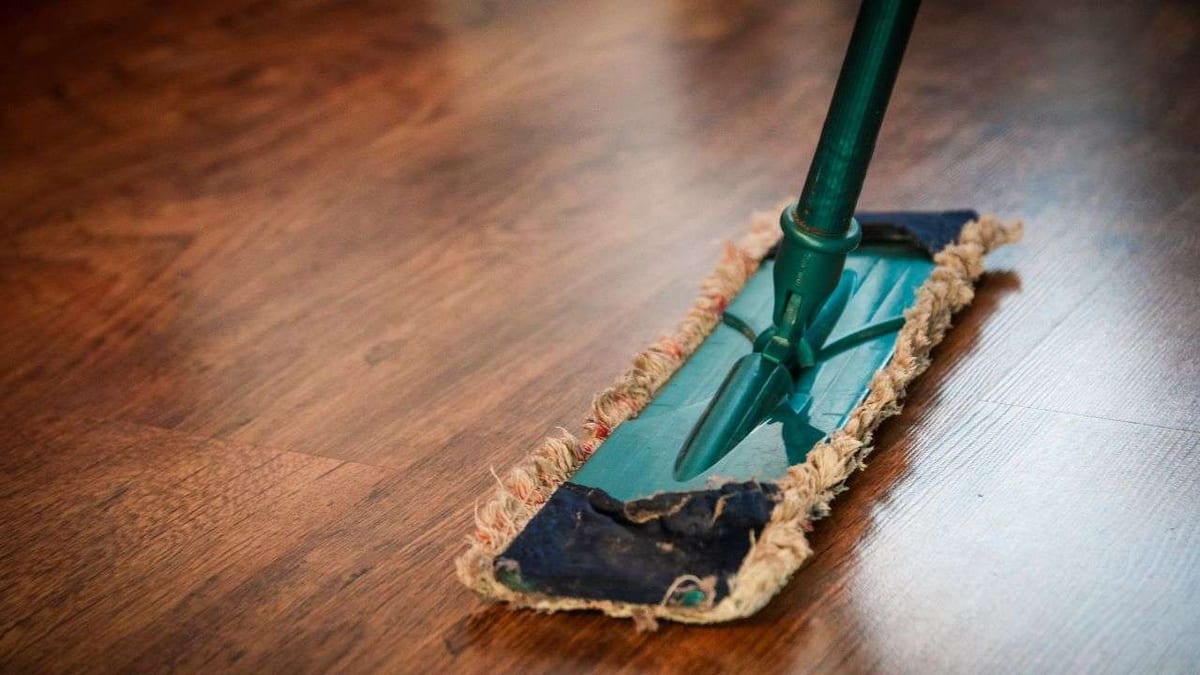 A flat microfibre mop cleaning a glossy dark wood floor.