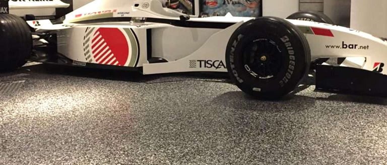 A white race car parked on a speckled grey epoxy flake garage floor with a glossy finish.