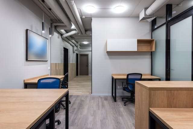 An office with light grey wood-look plank flooring, wooden desks and blue chairs.