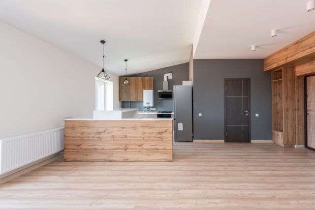 Light oak-toned flooring across an empty open-plan kitchen with a wood-panelled island and dark grey feature wall.