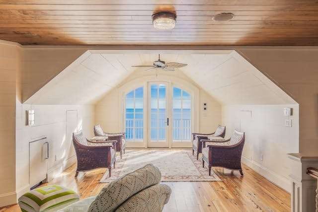 An attic sitting room with a pale pine floor, a wood-plank ceiling and arched French doors.