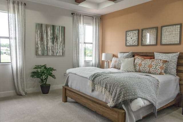 A bedroom with pale grey carpet, a wooden bed with layered bedding and framed art above.