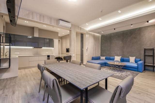 An open kitchen, dining and living space with light grey wood-look flooring and a blue sectional sofa.