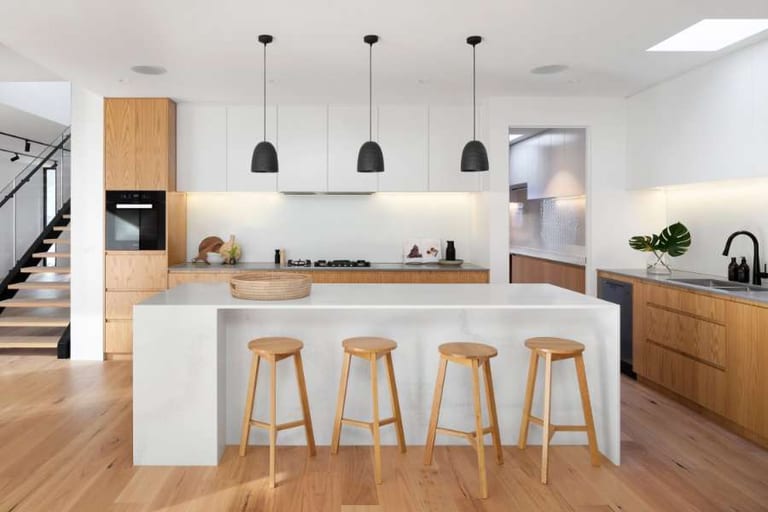 Light wood flooring in a modern white and oak kitchen with a waterfall-edge island and four wooden stools