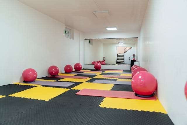 A fitness room with interlocking black, yellow and pink foam mats and exercise balls.