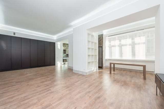 An empty room with light wood-look plank flooring, dark wall cabinets and a wooden bench.