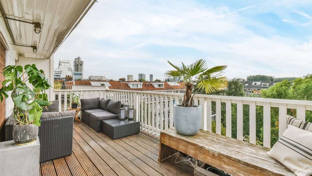 A rooftop balcony with wood decking, outdoor sofas and potted palms.