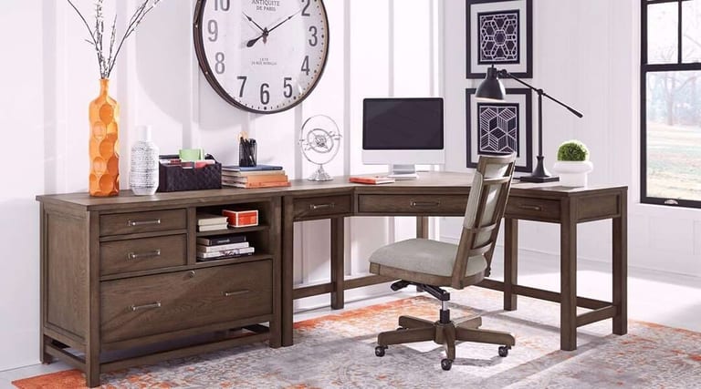 A dark wood desk and office chair on a patterned area rug in a home office, under a large wall clock