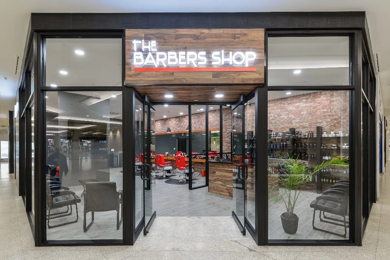 The Barbers Shop at West Edmonton Mall: the glazed shopfront under its illuminated sign, with a pale wood-look plank floor running out to the mall concourse.