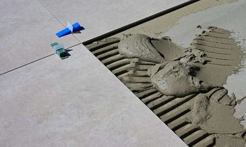 Large-format tile set into ridged thinset mortar with levelling clips at the joints.