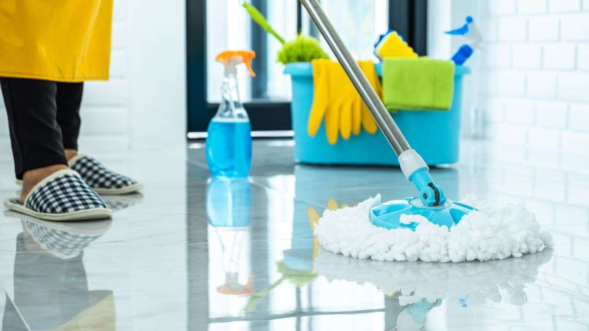 A spin mop cleaning a glossy tile floor beside a bucket of cleaning supplies.
