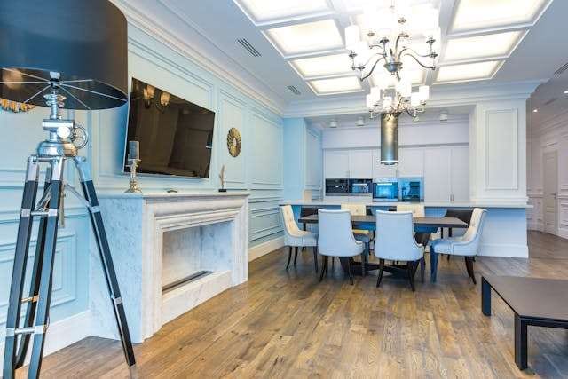 A pale blue panelled kitchen and dining room with a medium-brown wide-plank wood floor.