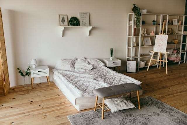 A bedroom with a warm pine plank floor, a low bed, a grey rug and white shelving.
