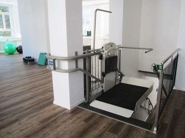A platform stair lift beside stairs in a room with dark wood-look plank flooring.