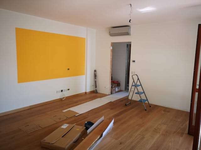 A room under renovation with a new medium-brown wood floor, a stepladder and flooring boxes.