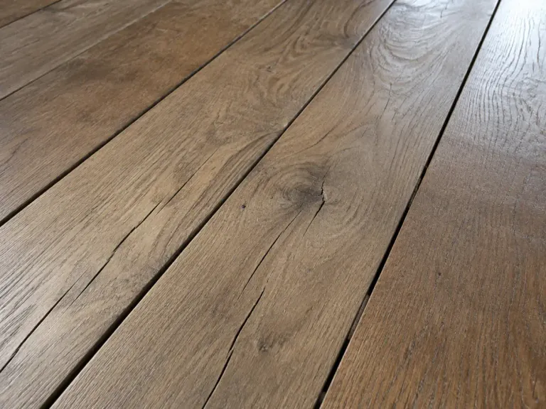 Close-up of dry hardwood floorboards with gaps between the boards and small cracks in the wood.