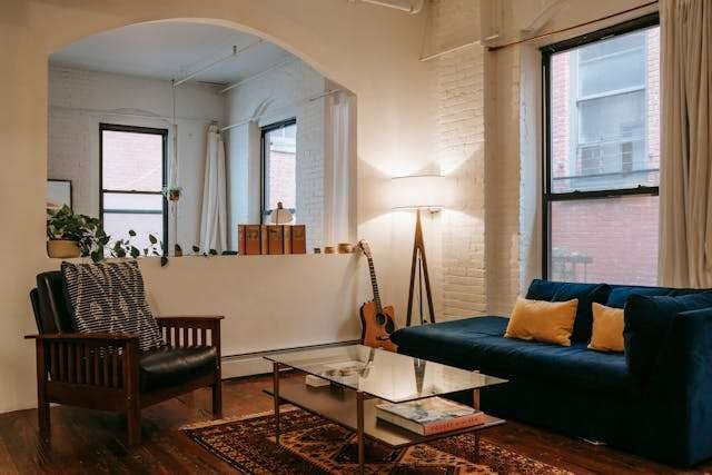 A loft living room with a dark wood floor, a navy sofa, a patterned rug and tall industrial windows.