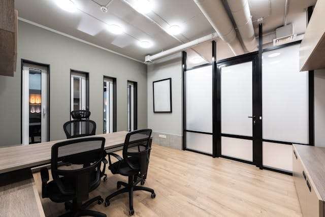 An office with light wood-look plank flooring, a desk with black mesh chairs and frosted glass doors.
