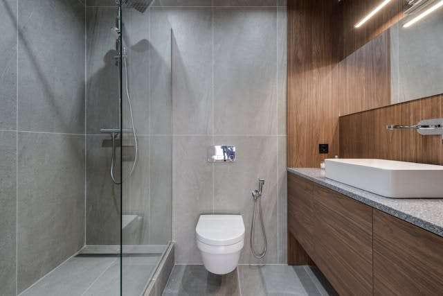 A bathroom with a walk-in glass shower, grey large-format tile and a wood-grain vanity.