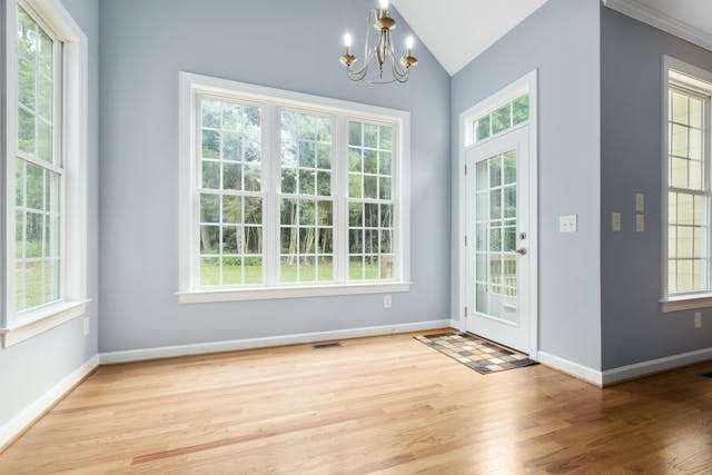 An empty sunroom with a light hardwood floor, pale blue walls and large windows.
