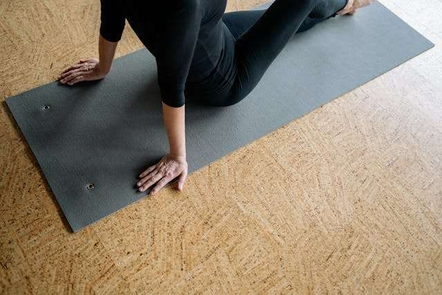 A person stretching on a grey yoga mat laid over a cork floor.