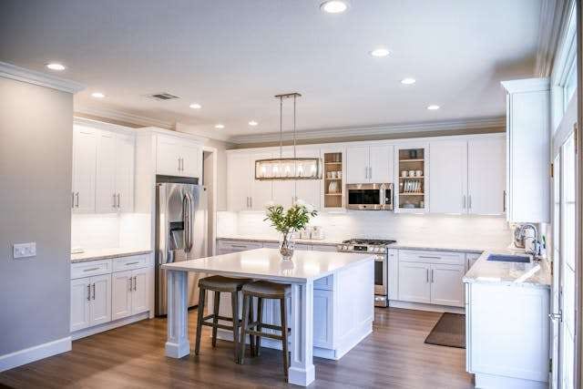 A white kitchen with an island, pendant lights and a dark wood-look plank floor.
