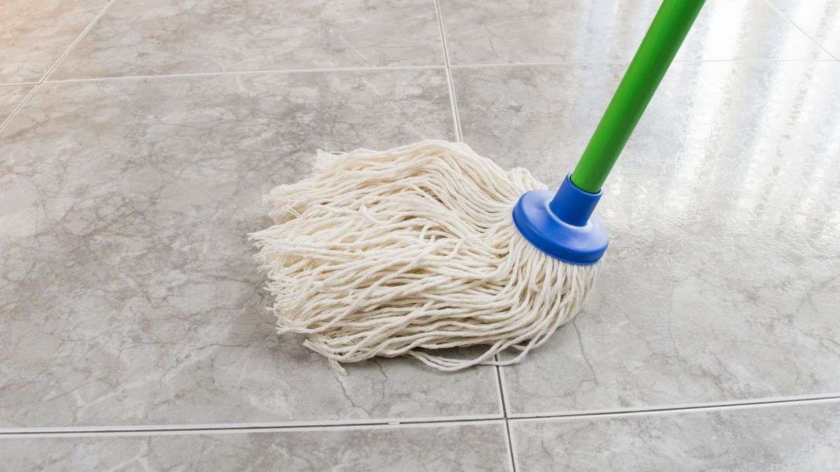 A string mop cleaning a grey marble-look tile floor.