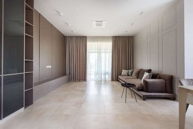 A long living room with pale large-format porcelain tile, a low sofa and dark wall panelling.