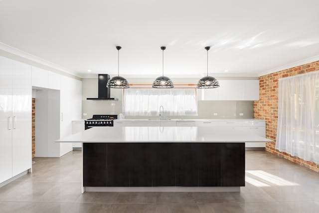 A large white kitchen with a dark island, pendant lights and grey large-format tile.
