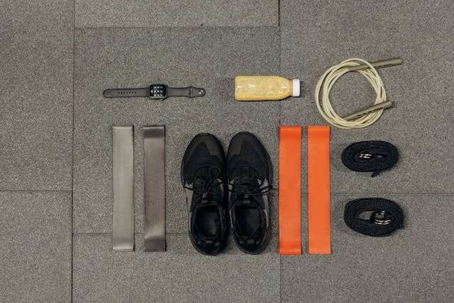 Workout gear, sneakers and resistance bands laid out on grey rubber gym flooring.