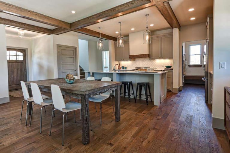 Dark oiled oak hardwood in an open dining area and kitchen with a rustic table and beamed ceiling