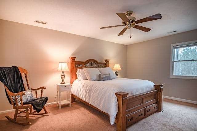 A bedroom with beige carpet, a wooden sleigh bed and a rocking chair.