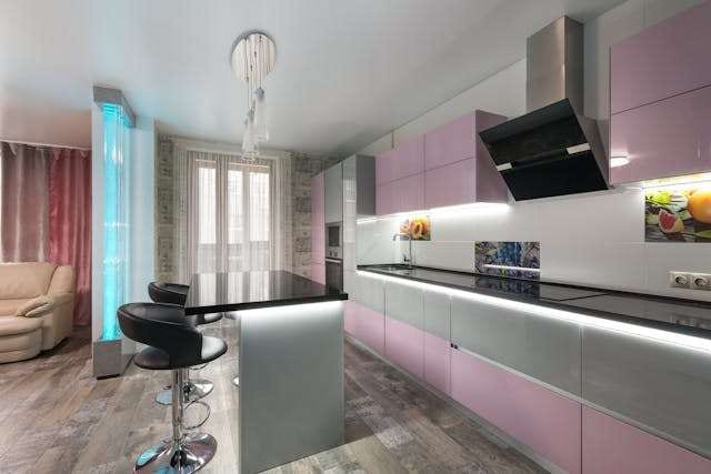 A kitchen with pink cabinets, a black island counter and grey wood-look flooring.