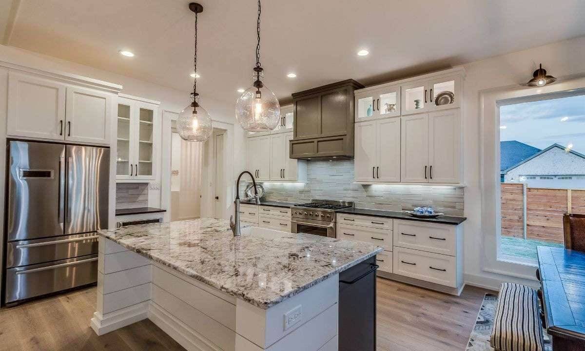 A white kitchen with a granite-topped island, glass pendant lights and a wood-look floor.
