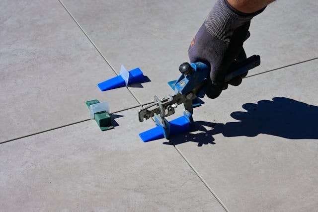 A gloved hand tightening a tile levelling clip between large-format grey floor tiles.