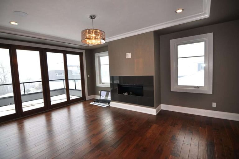 Dark brown hardwood flooring in an empty living room with a linear fireplace and floor-to-ceiling windows.