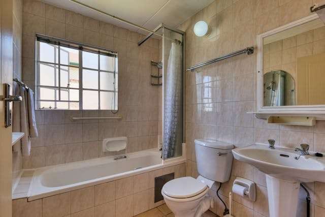 A dated bathroom with beige wall tile, a bathtub and a pedestal sink.