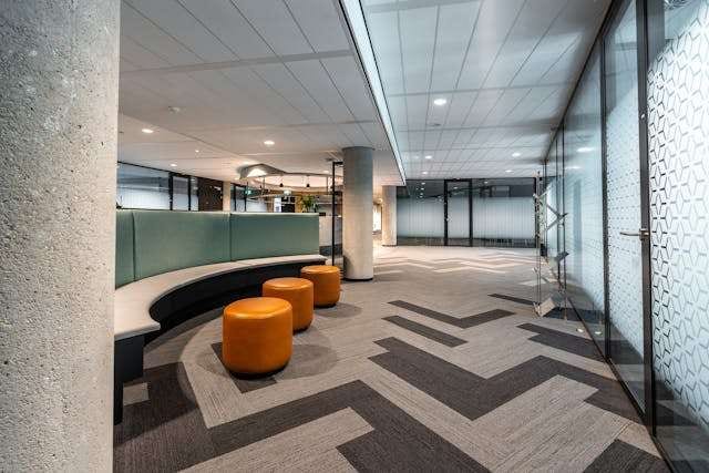 Grey and beige patterned carpet tile in an office lobby with curved bench seating and orange stools.