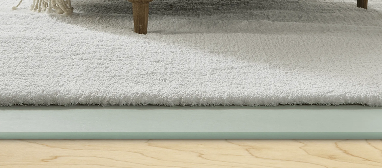 Cutaway of a plush cream carpet over a foam underlay pad on a wood subfloor.